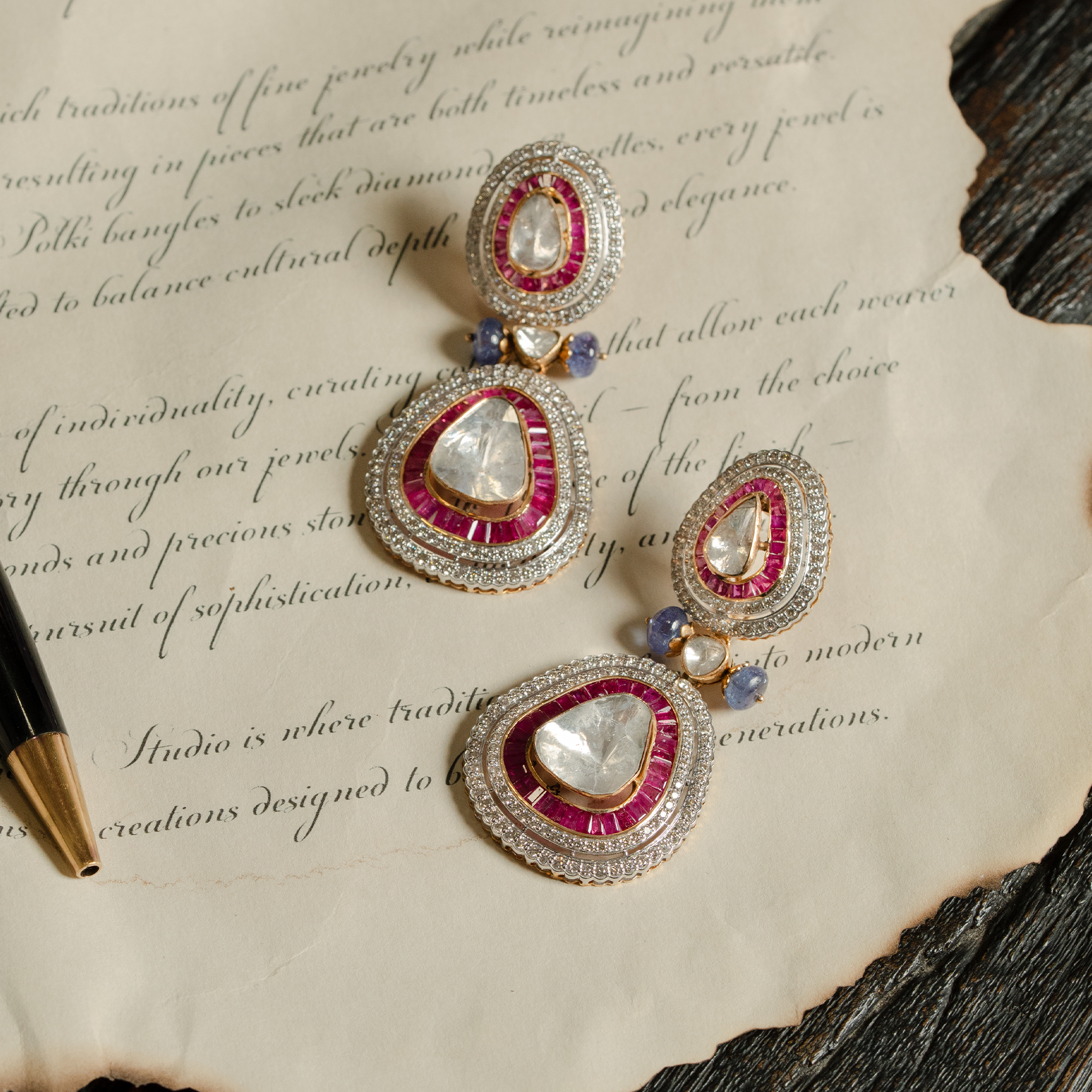 A pair of vibrant teardrop earrings featuring large triangular polki diamonds encased in ruby baguettes and shimmering pavé halos, accented with delicate blue sapphire beads.