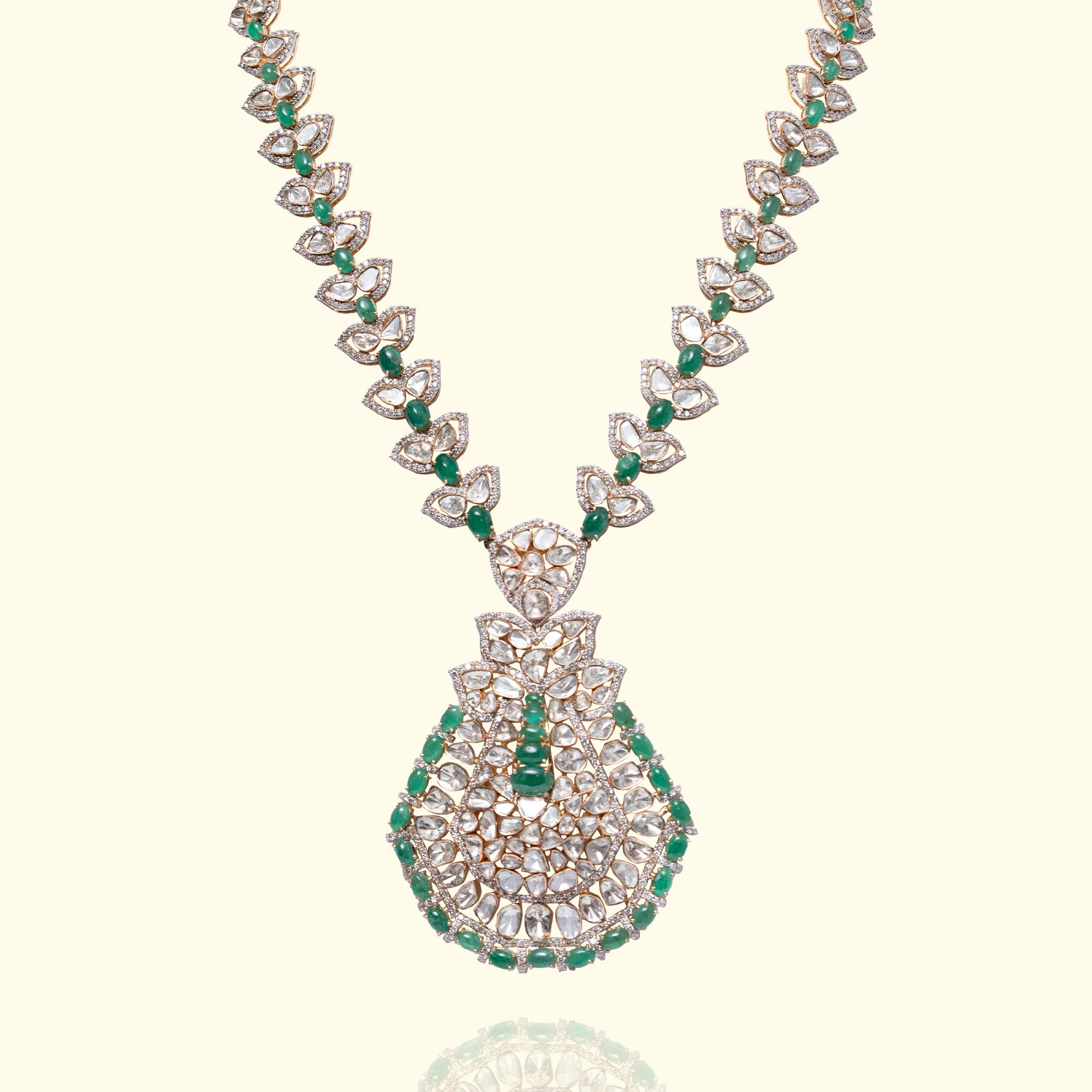 A magnificent long necklace featuring a chain of leaf-motif polki diamond links accented with emerald beads, leading to an oversized, pear-shaped mosaic pendant of polki diamonds and vibrant emerald beads in india