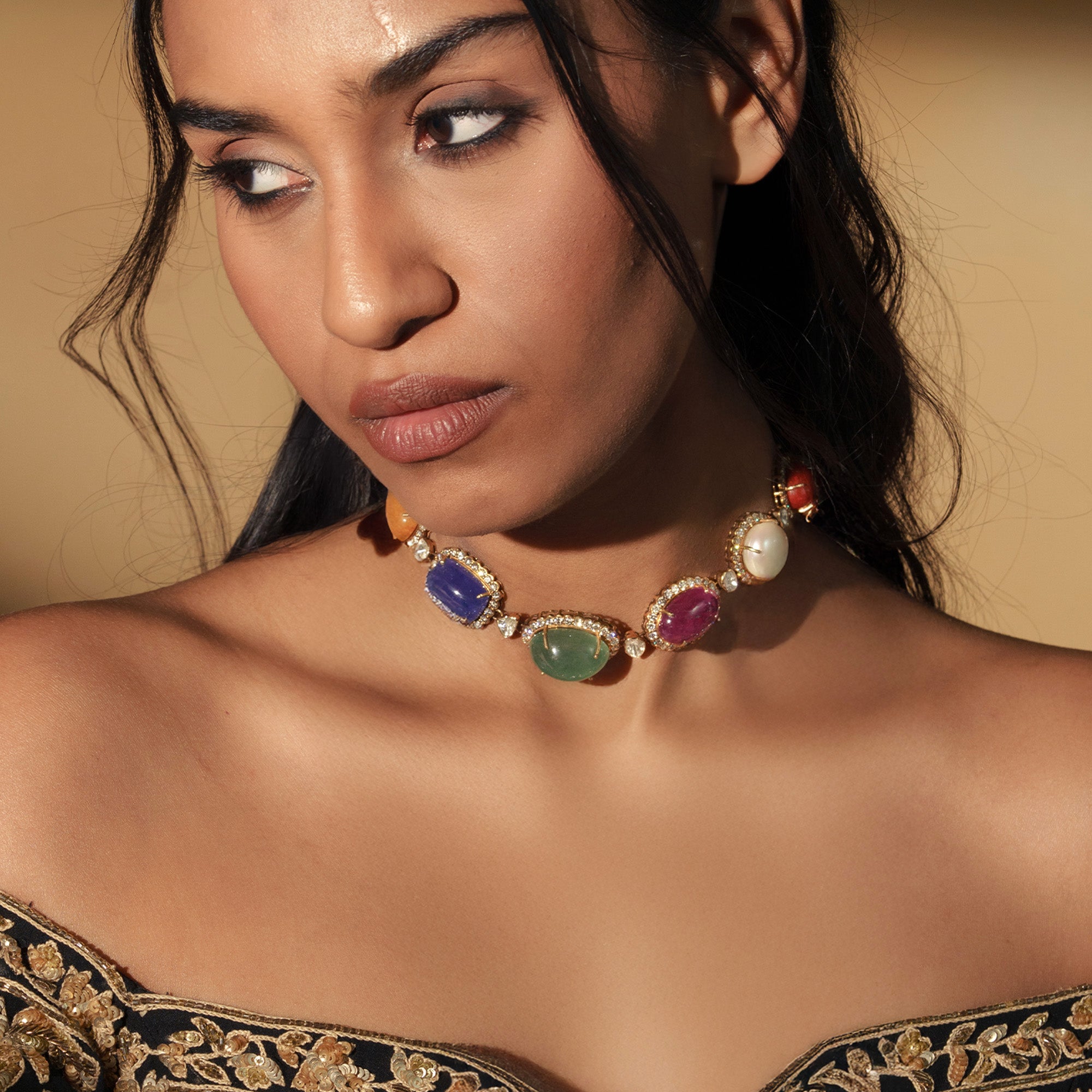 A model wearing a vibrant polki choker featuring a series of large, oval navratan gemstone—including tanzanite, emerald, ruby, and pearl, etc—each encircled by a halo of shimmering pavé diamonds and linked with unut diamond.