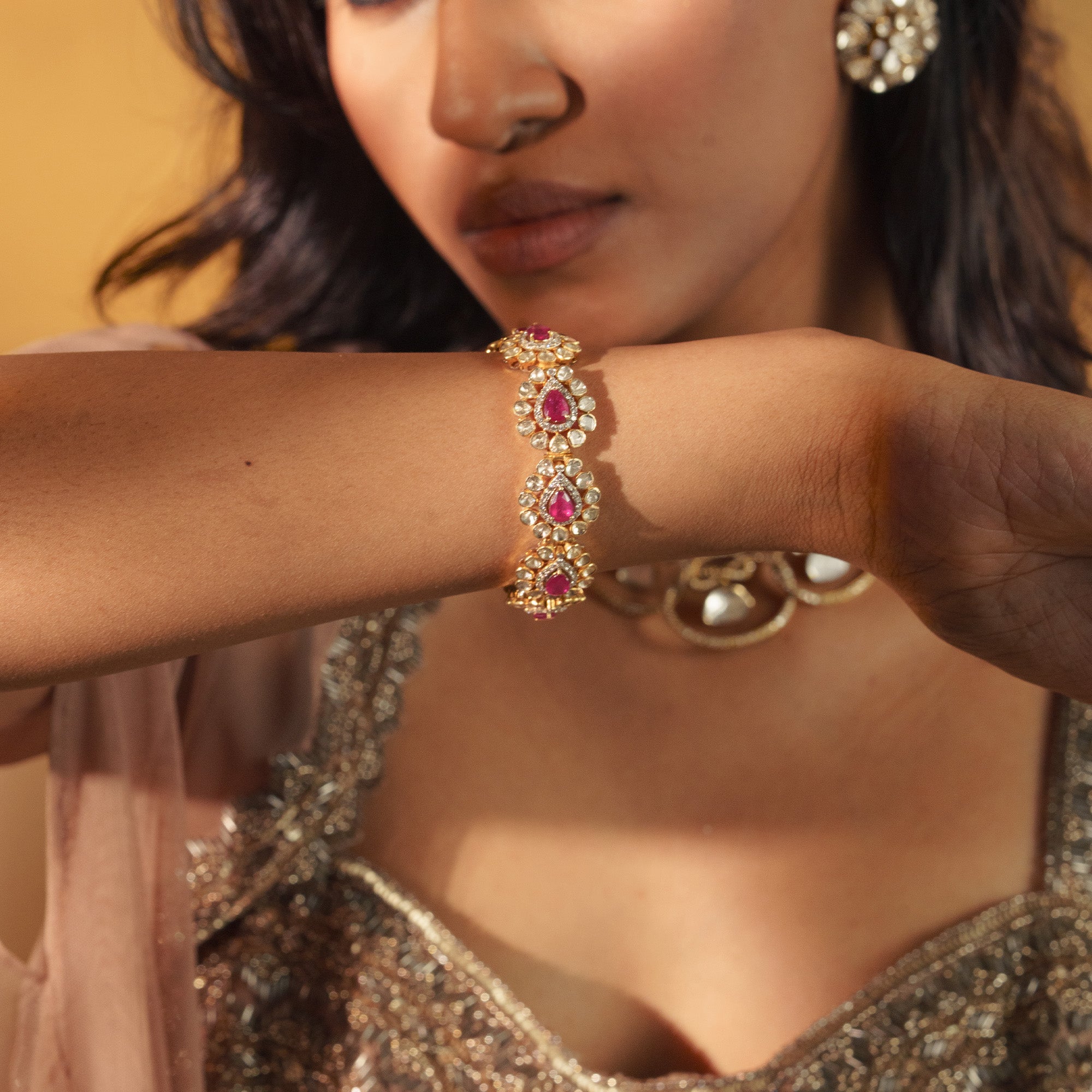 Close-up of a model wearing a gold ruby and Polki diamond link bracelet paired with a shimmering gold embroidered outfit.
