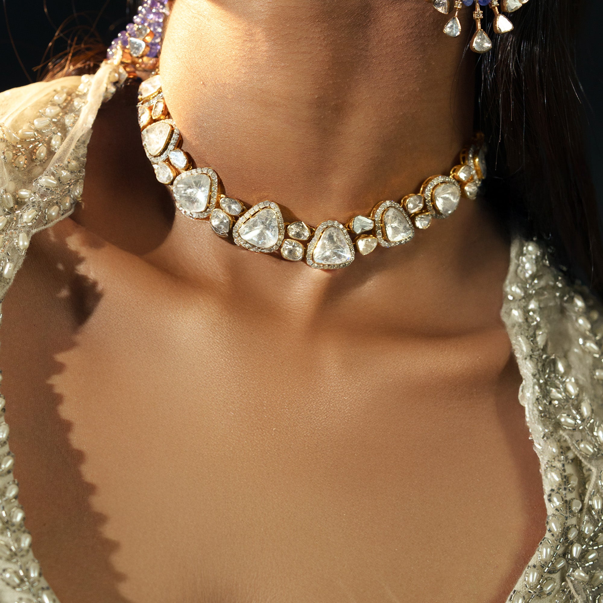 A model wearing a sophisticated gold choker necklace featuring a graduating sequence of triangle-cut polki diamonds in individual diamond-pavé frames, styled elegantly with a beaded ivory ensemble.
