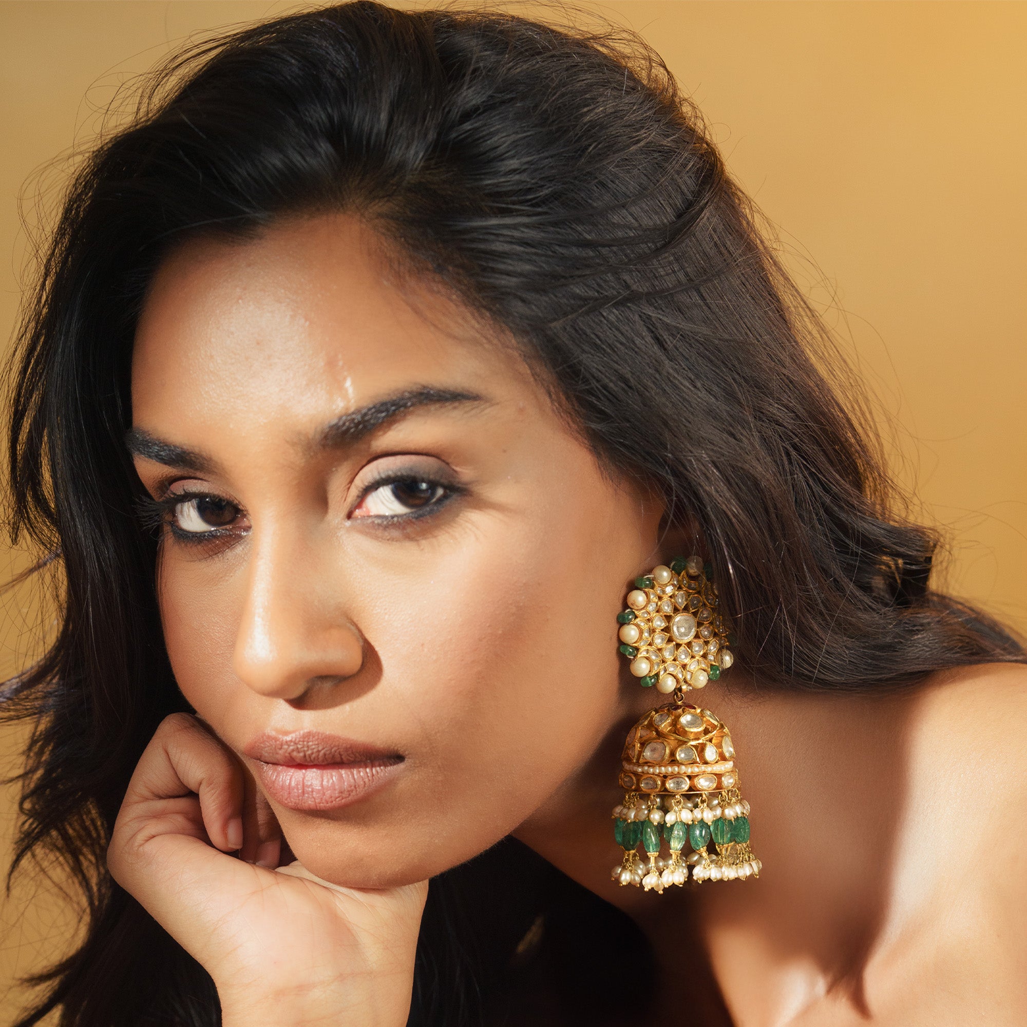 Editorial portrait of a model wearing large gold Polki Jhumka earrings with floral studs, bell-shaped drops, and a fringe of emerald beads.