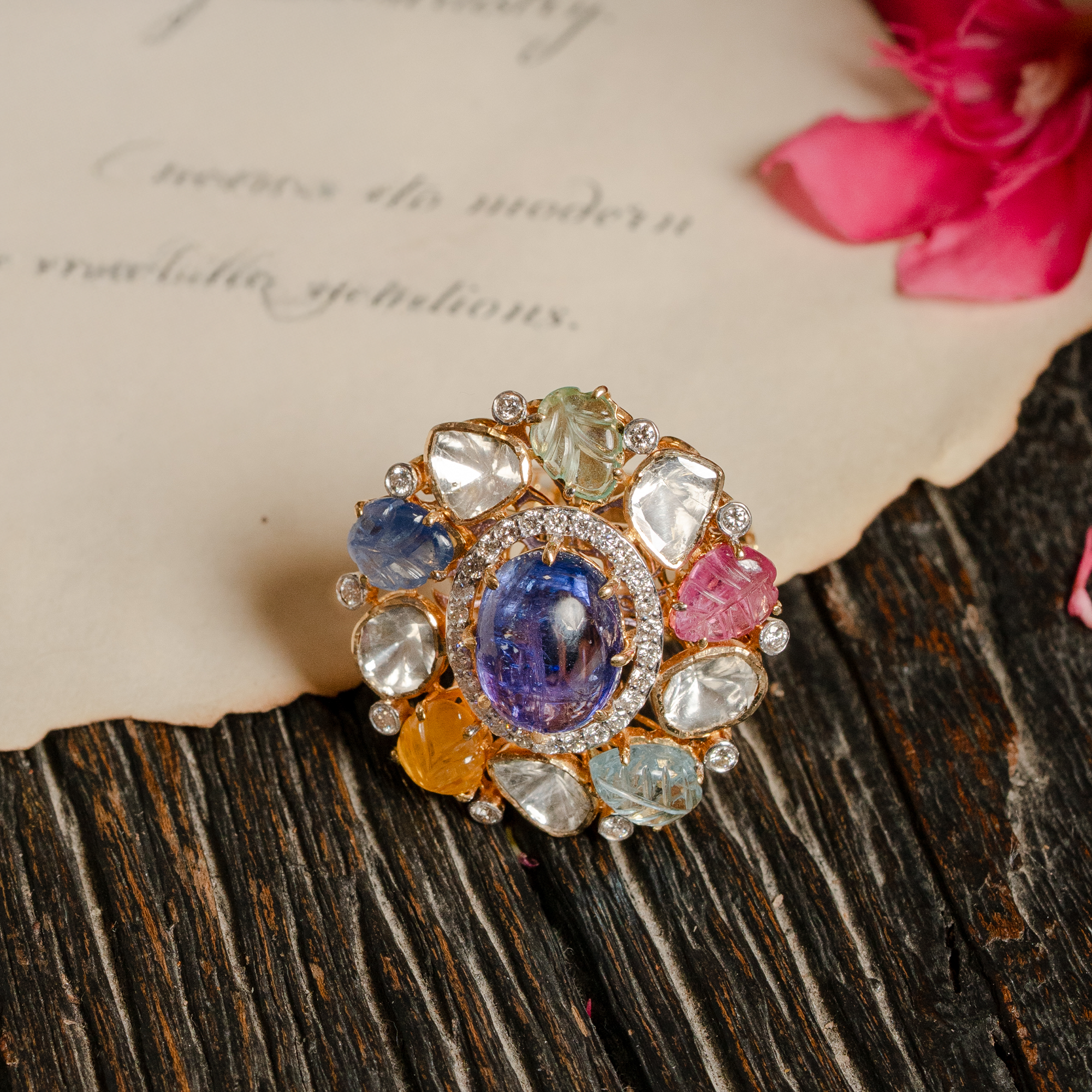 Luxurious gold Polki diamond cocktail ring centered with a large oval tanzanite cabochon, surrounded by carved multi-colored navratan gemstones including ruby and sapphire, emerald, tanzanite, yellow sapphire accented with a diamond-pave halo.