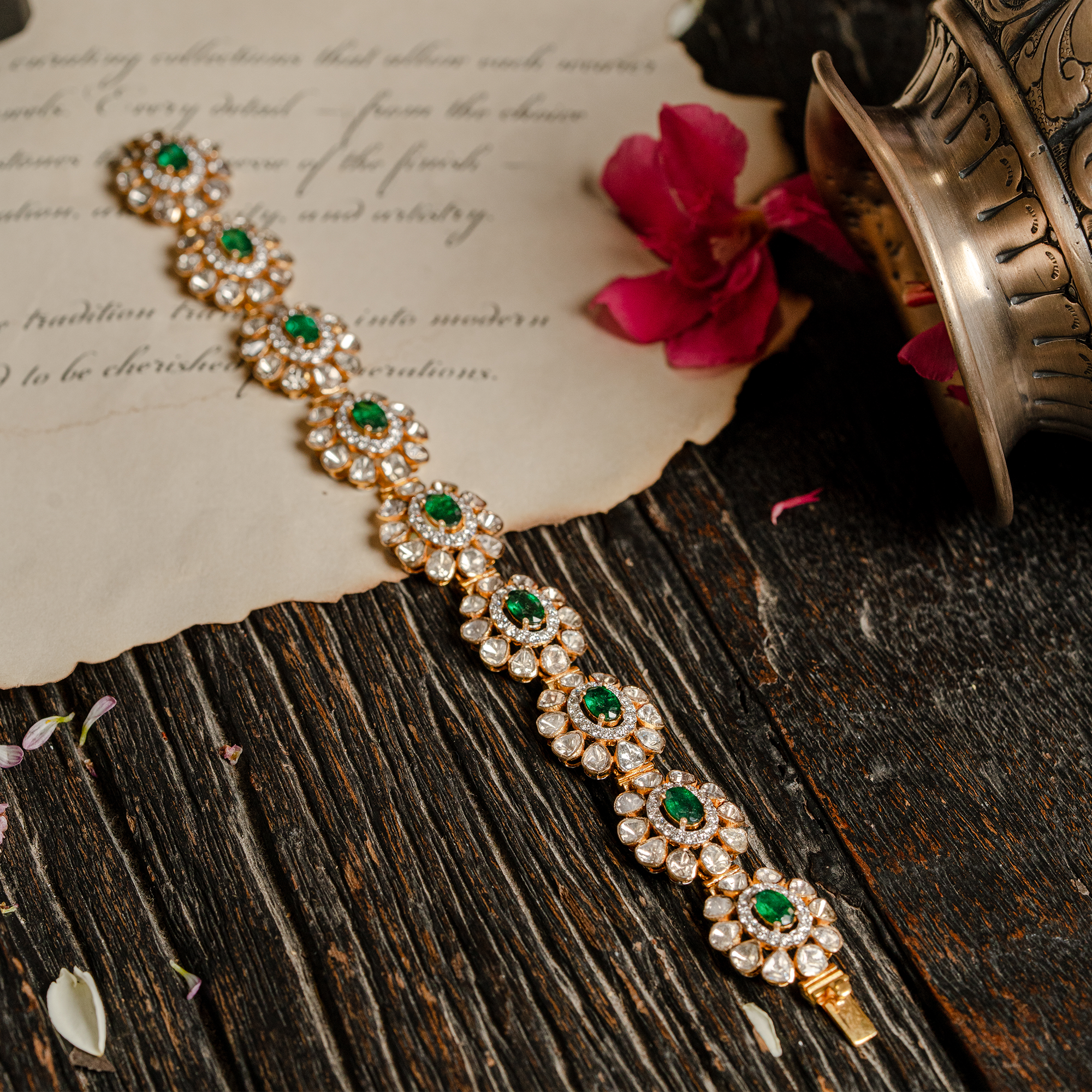 A delicate gold tennis-style bracelet featuring oval-cut emerald centers surrounded by sparkling polki diamond petals in a continuous floral link design in india