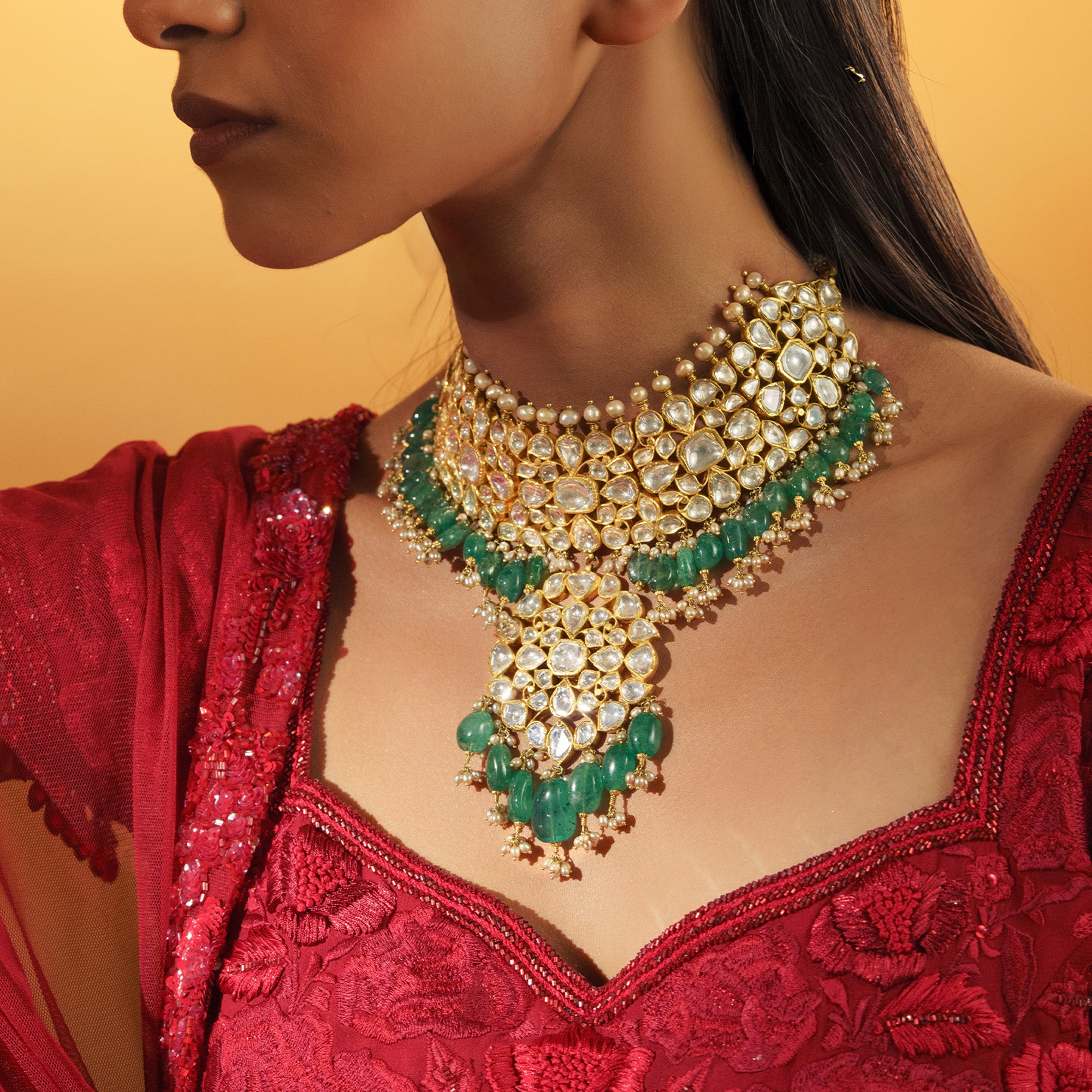 Woman wearing a gold and green necklace with a red top against a yellow background in india