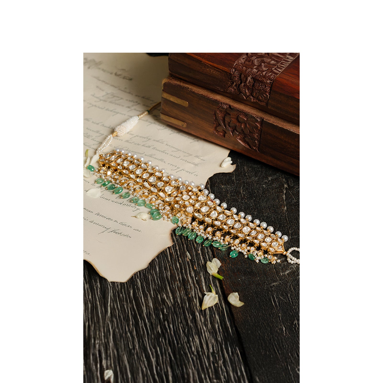 A magnificent high-glamour look featuring a pearl-strung polki choker layered with a wide, tiered gold bib necklace encrusted with teardrop polki diamonds and a lush emerald fringe.