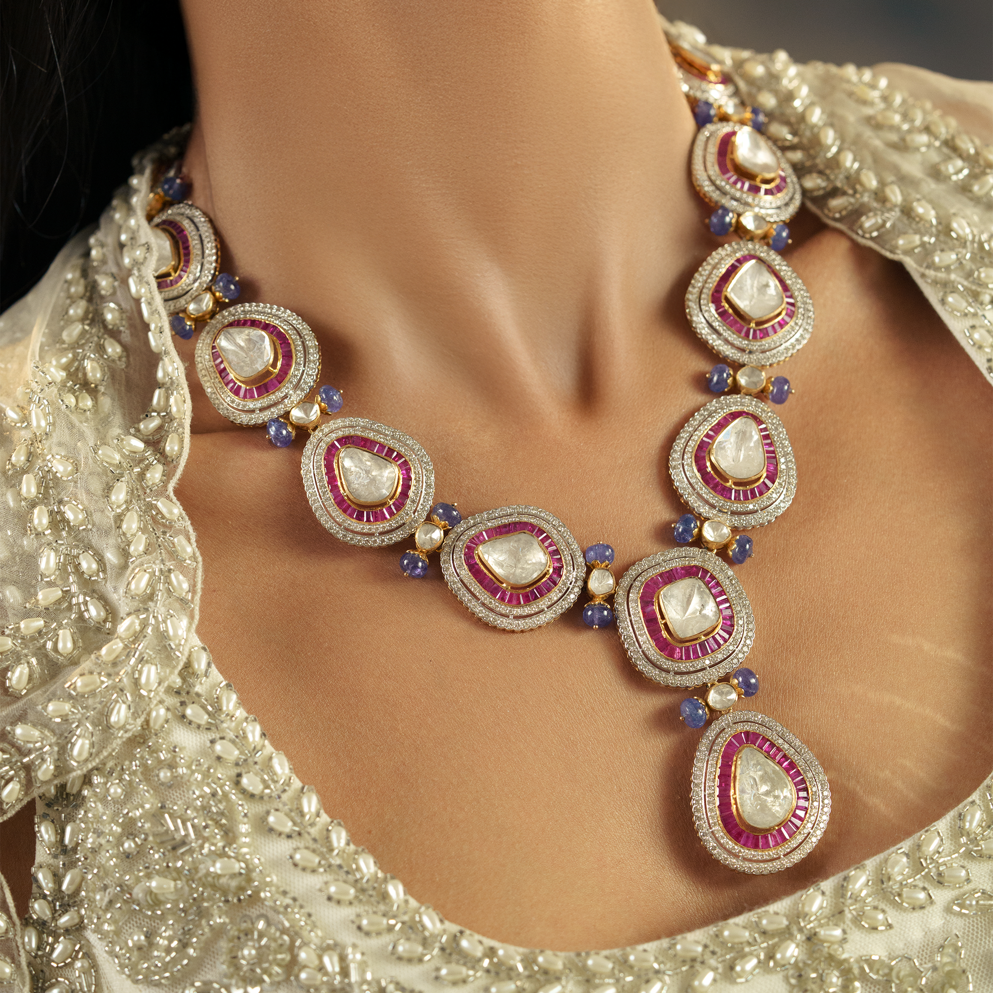 Close-up of a model wearing a massive gold statement necklace with large pear-shaped Polki diamonds, channel-set ruby borders, and sapphire bead accents.