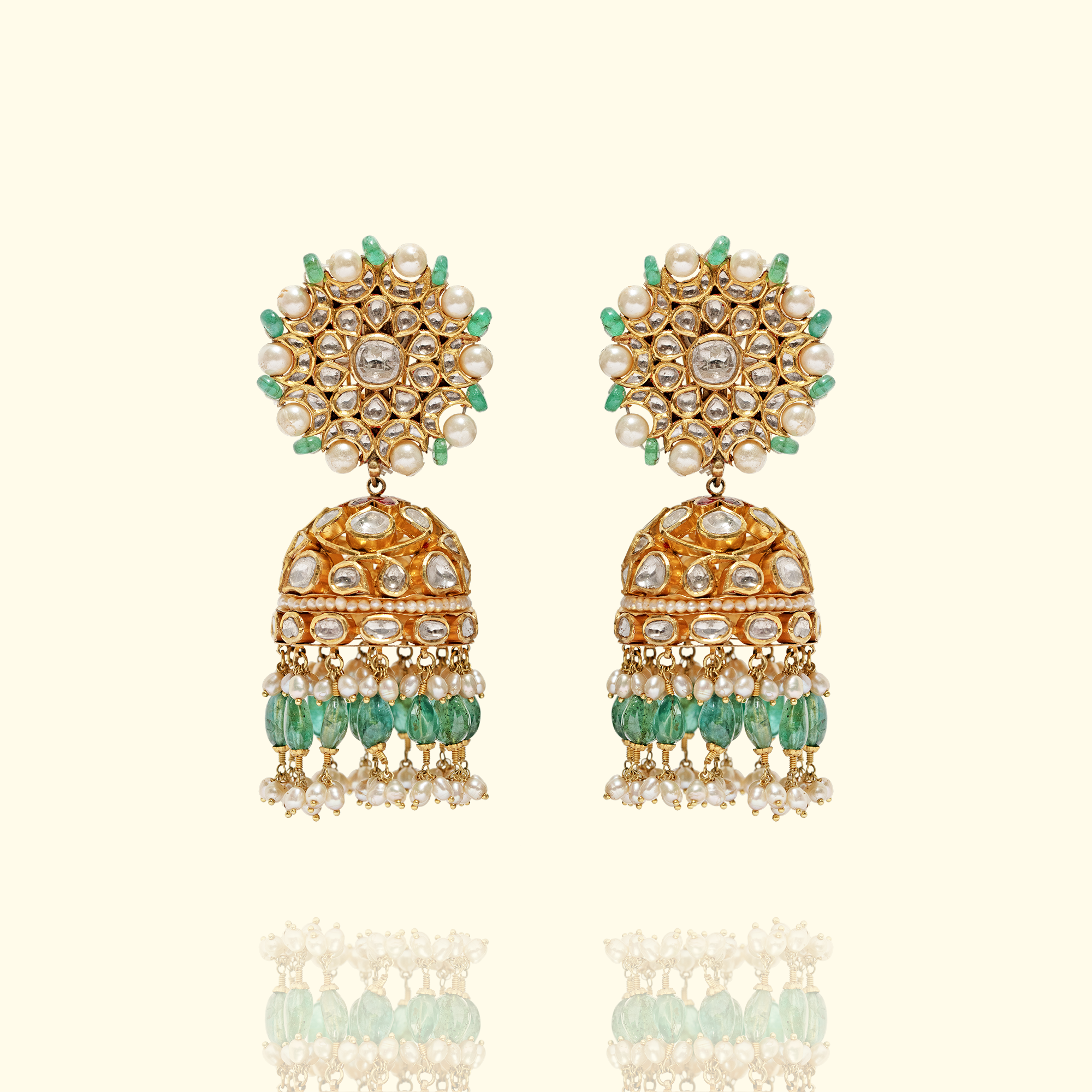 Pair of traditional gold Polki Jhumka earrings featuring floral-motif studs set with uncut diamonds, pearls, and emerald accents, finished with bell-shaped, jhumka, dome-shaped drops and a fringe of emerald beads and seed pearls.