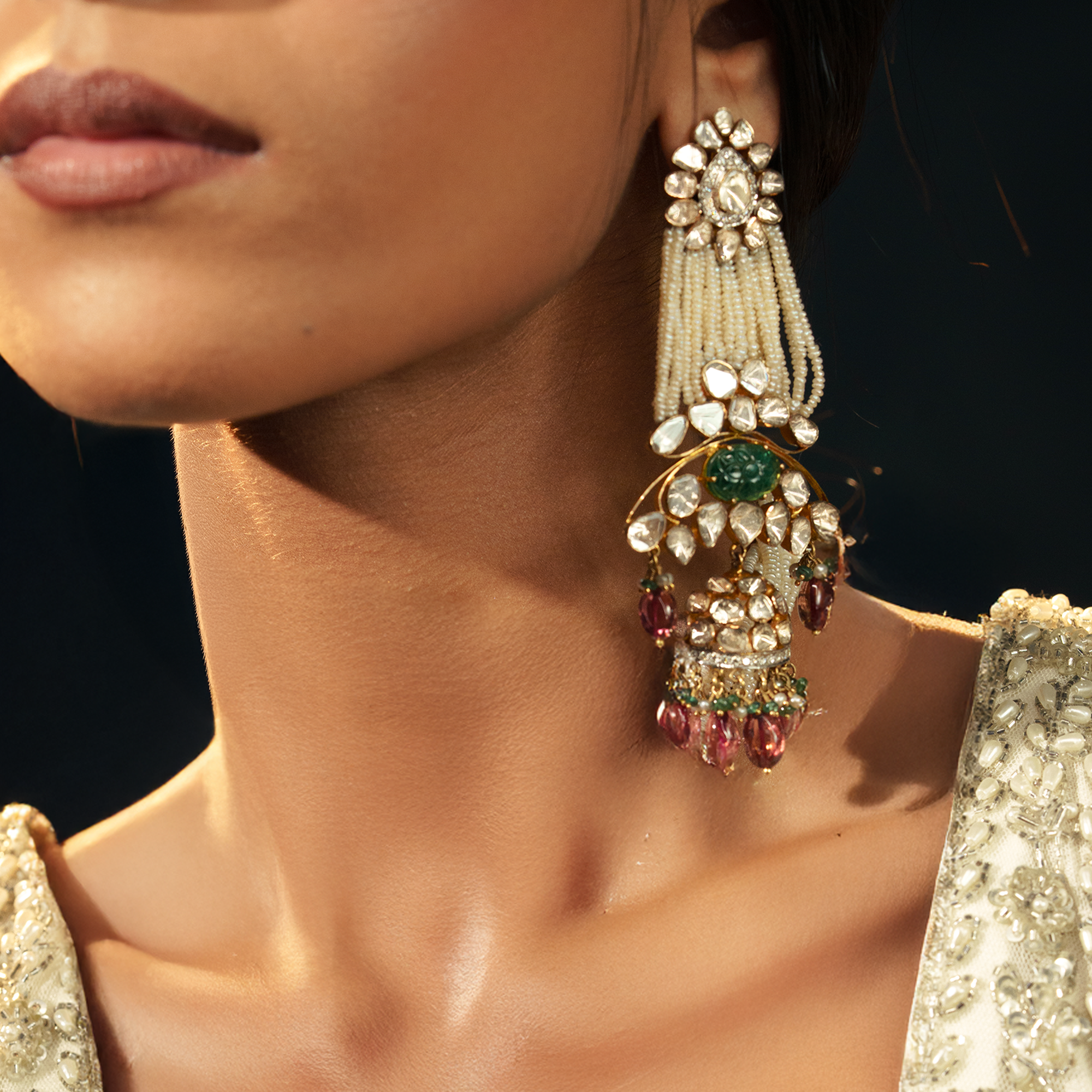 Editorial portrait of a model wearing long, elaborate pearl and Polki Jhumka earrings featuring multi-strand seed pearl tassels and an emerald center stone.
